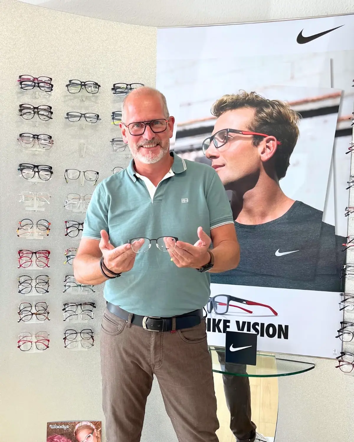 Augenoptiker zeigt eine Brillenfassung vor der Fassungswand
